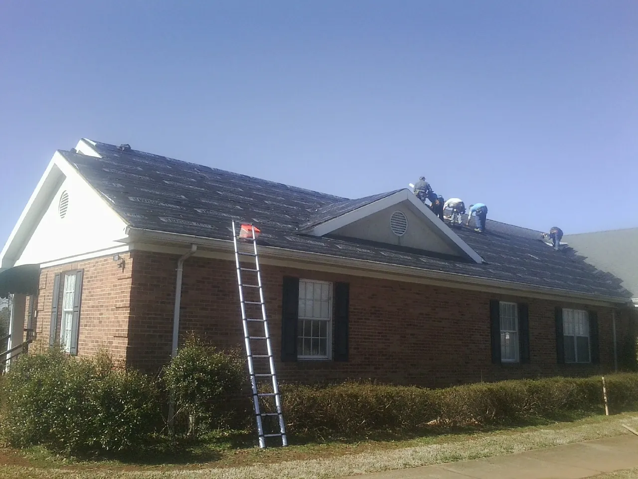 Crew tearing shingles off a brick ranch roof with a ladder set — Emergency Roof Repair work by our crew in Bonanza